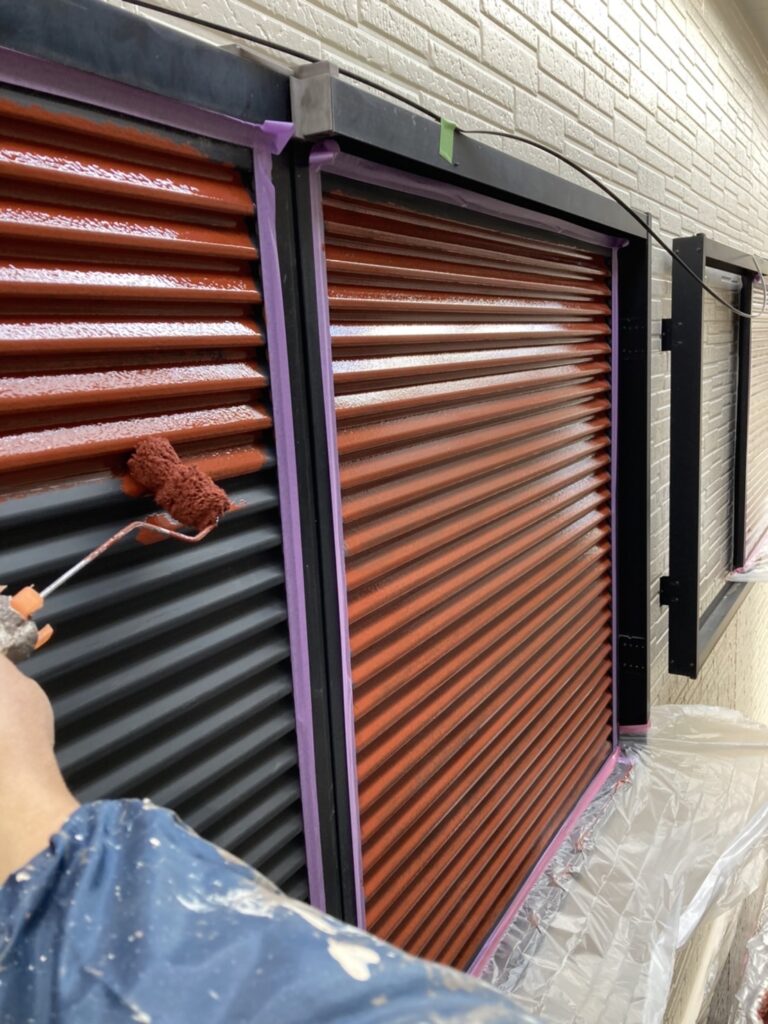 雨戸に赤茶色の錆止め塗料を塗布している様子