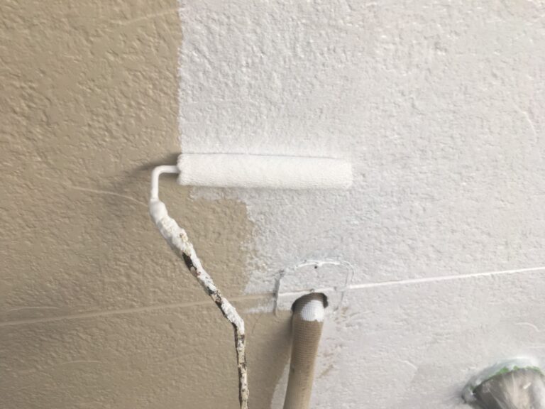 外壁の下塗り作業。茶色のサイディング外壁に白い下塗り材（リフレッシュサフェーサーエポ）をローラーでたっぷりと塗布し、下地を強化している様子