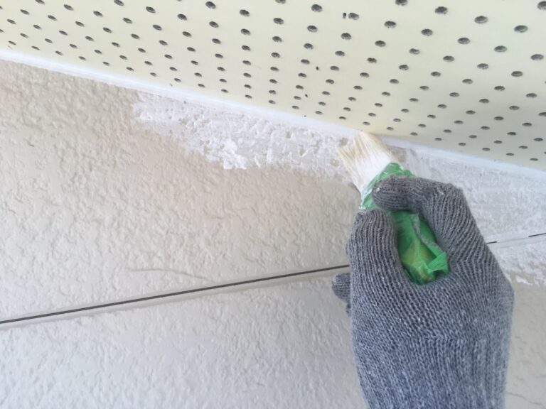 軒天と外壁の境目（入隅）を刷毛で塗装する様子。ローラーが届かない細かい部分を先に塗る「ダメ込み」作業で塗り残しを防ぐ