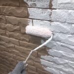 サイディング外壁の凹凸に合わせてローラーで下塗りを進める職人。塗りムラがないよう、均一な厚みで白い下塗り層を作っていく