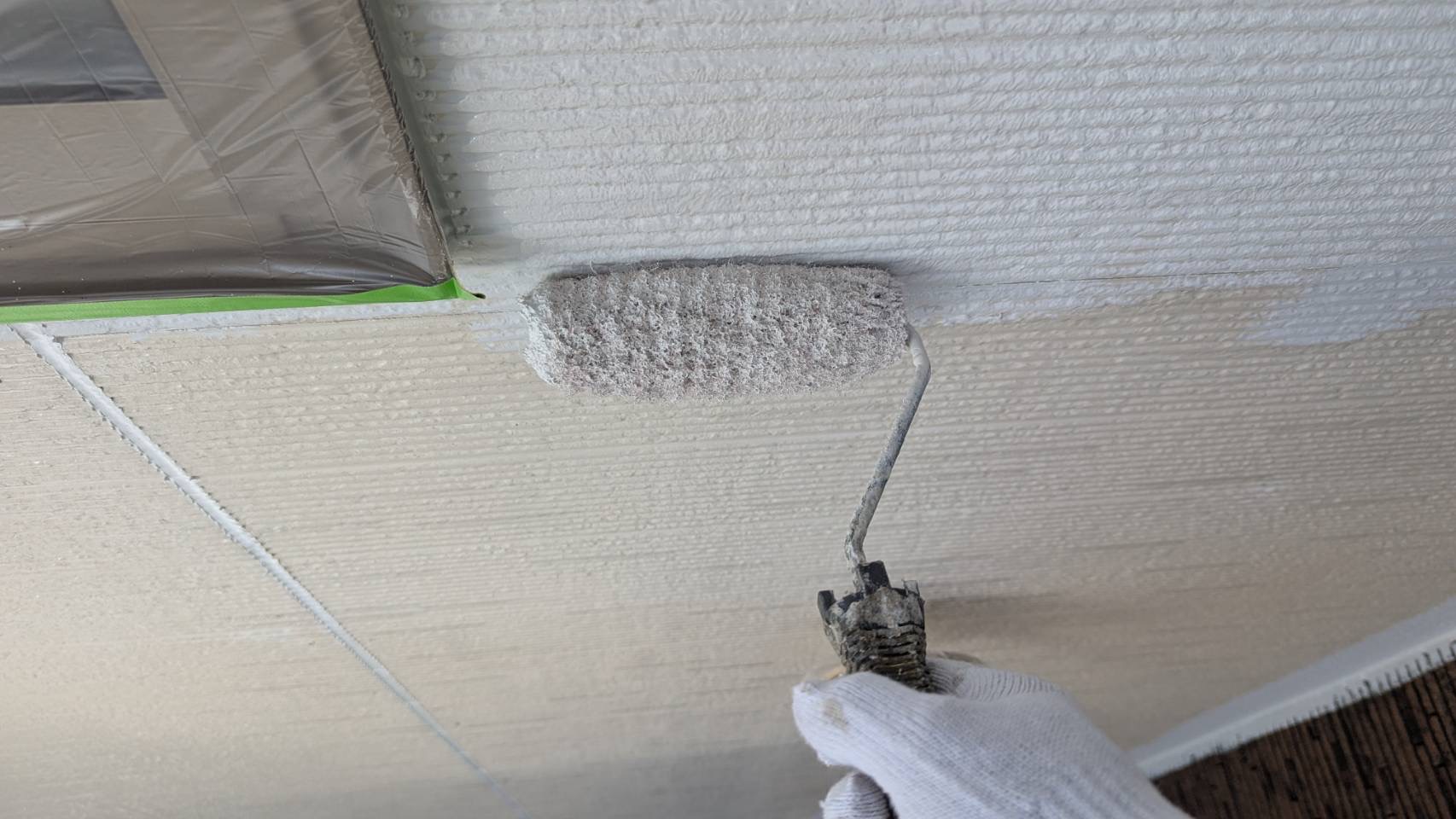名張市S様邸の外壁塗装、窓まわりを養生してナノウォール15をローラーで中塗りしている様子